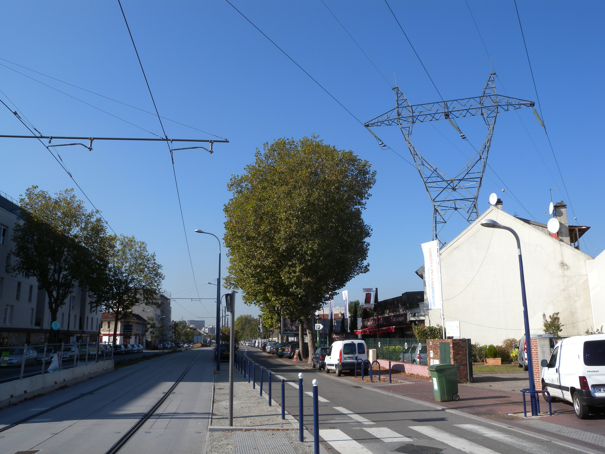 La ligne de tramway circule dans l’espace de l’avenue, sur les bords de laquelle se côtoient des formes bâties contrastées, et un alignement d’arbres décimé par endroits.